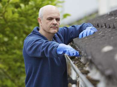 En mann med blå gummihansker renser en takrenne for løv (Foto)