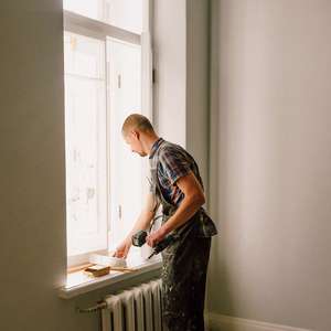 Håndverker står og sparkler en vinduslist (Foto)