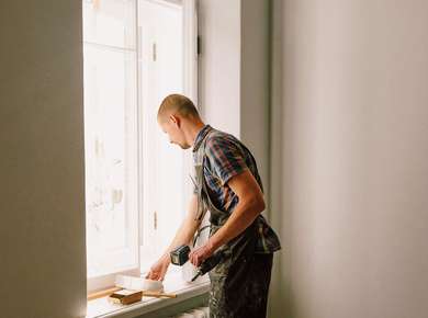 Håndverker står og sparkler en vinduslist (Foto)