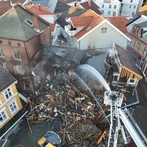 Et nedbrent hus i et tettbygd bystrøk spyles med vann fra en kranbil for å stoppe eventuell ulmebrann (Foto)