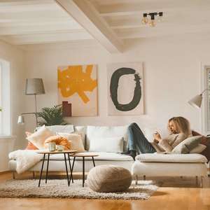 Kvinne ligger i sofaen med mobiltelefonen i en lys og åpen stue (Foto)