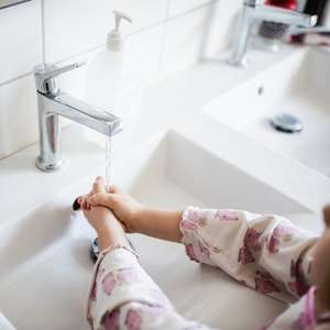 Et barn vasker hendene sine under en kran med rennende vann
