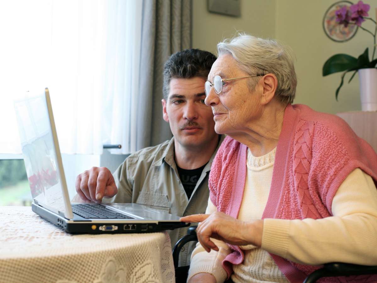 Mann hjelper eldre kvinne med bruk av PC