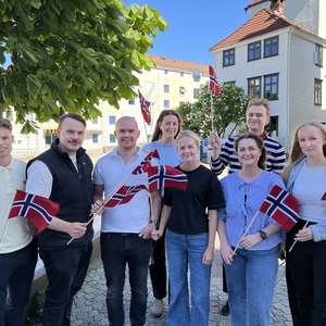 Ansatte i kundeservice fra Frende står i brosteinsbelagt gate og vinker med norske flagg (Foto)