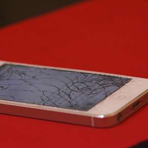 En mobiltelefon med knust skjerm ligger på et bord (Foto)