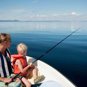 Mor og barn sitter med en fiskestang i en båt på stille sjø (Foto)