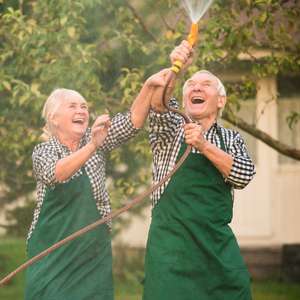 Et eldre par ler og leker med en hageslange i hagen - mannen holder hageslangen i været og spyler rett opp (Foto)