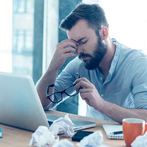 En mann sitter foran en PC og tar seg til hodet i fortvilelse