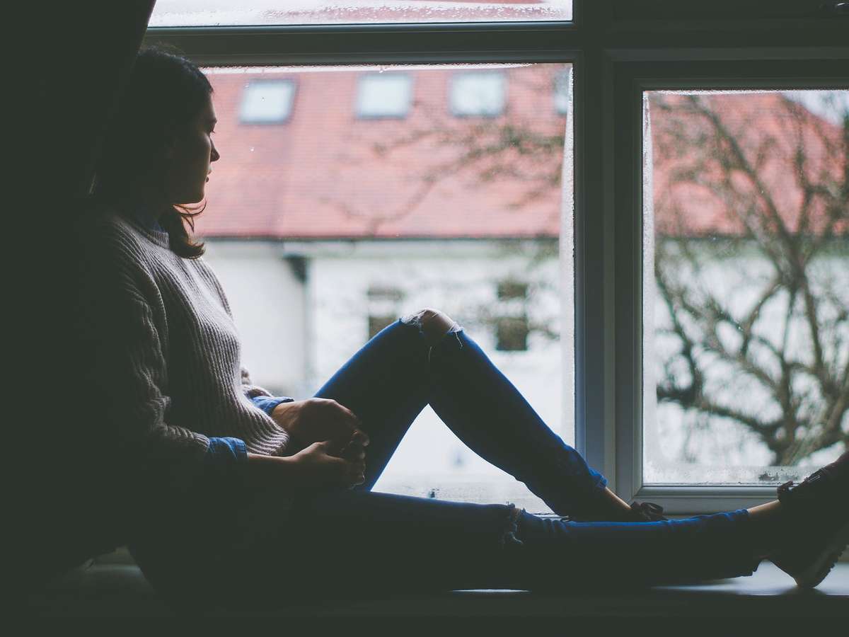 Ung kvinne sitter i vinduskarmen og ser ut