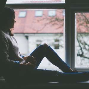 Ung kvinne sitter i vinduskarmen og ser ut