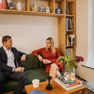 To kollegaer sitter i en sofa og diskuterer med en kopp kaffe i hånden (Foto)