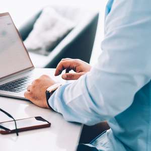 En mann sitter å jobber ved en PC, med brillene og mobilen liggende ved siden av (Foto)