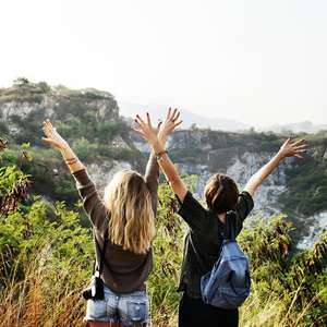 To ungdommer på reise strekker hendene i været med ryggen til mens de ser på en flott utsikt (Foto)