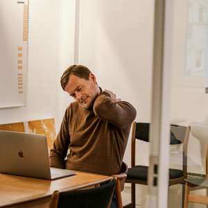 Mann som sitter tar seg til skulderen, og lener hodet til siden med et uttrykk av ubehag (Foto)