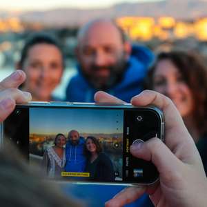 En person tar bilde av tre andre personer fra et utsiktspunkt med en telefon (Foto)