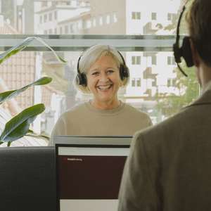 En kundeservice medarbeider på jobb smiler til kamera mens hun snakker i headsettet (Foto)